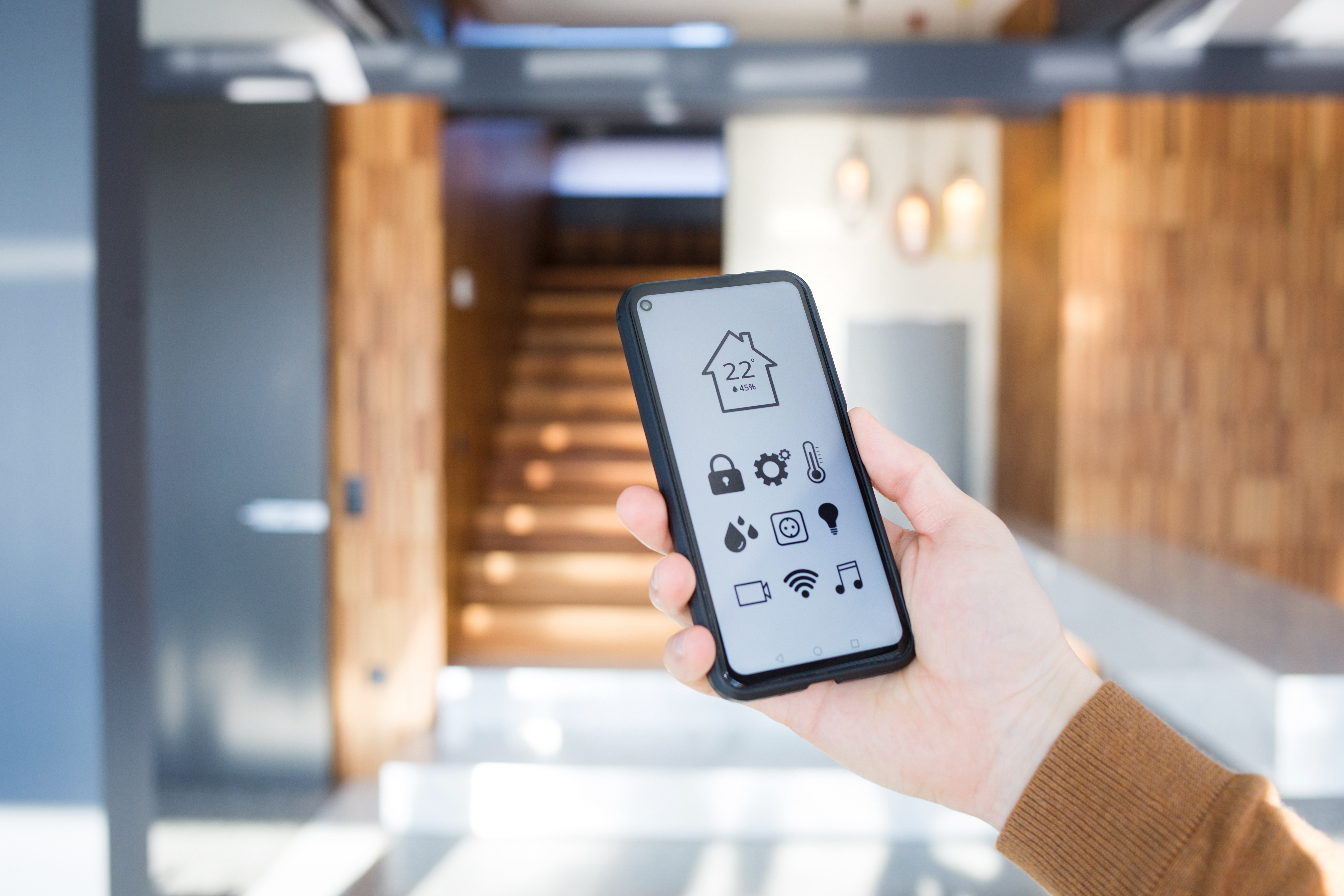 man controls smart home devices using app for mobile phone on background of interior of house.